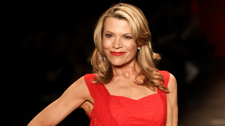 Vanna White porte une robe rouge avec du rouge à lèvres sur fond noir.