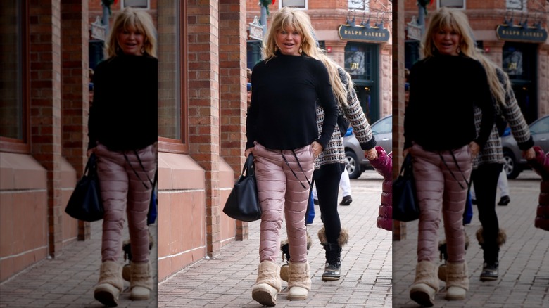 Goldie Hawn marche avec un pantalon de neige rose matelassé et un pull noir