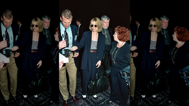 Meg Ryan photographiée portant un tailleur-pantalon bleu marine avec une chemise rayée et des lunettes de soleil.