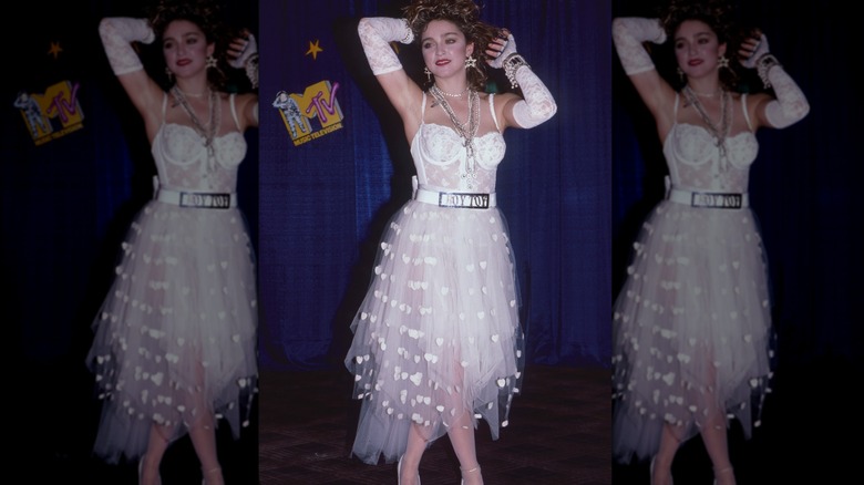 Madonna posant aux MTV Video Music Awards portant une robe en dentelle blanche, des gants en dentelle blanche et plusieurs colliers et bracelets.