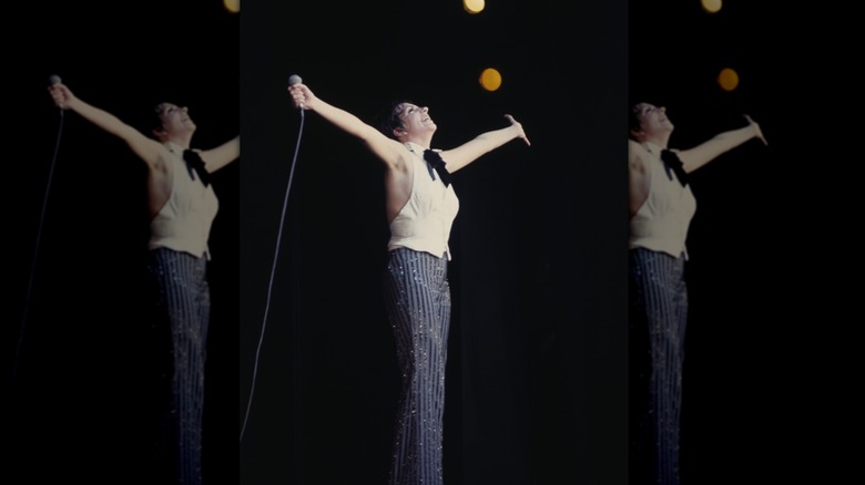 Liza Minnelli se produisant sur scène avec un microphone à la main et les mains en l'air.