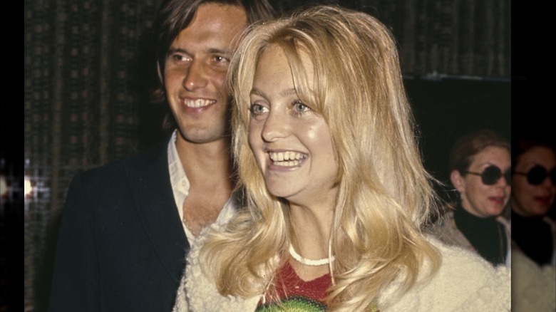 Goldie Hawn souriante sans maquillage, portant un pull blanc et un collier blanc.