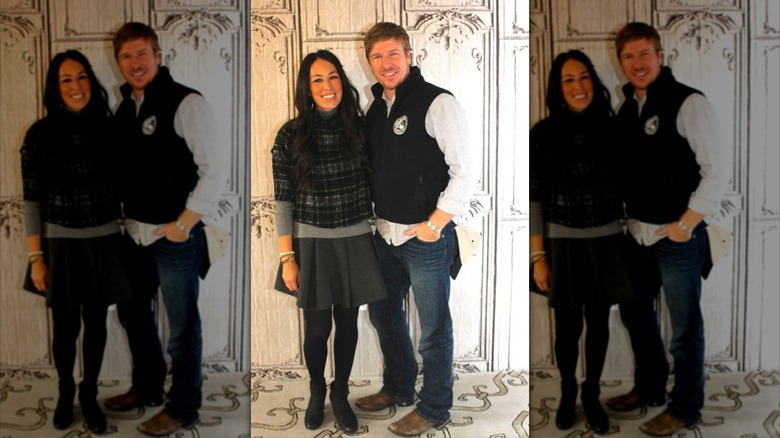 Joanna Gaines et Chip Gaines posant ensemble devant un mur blanc orné.