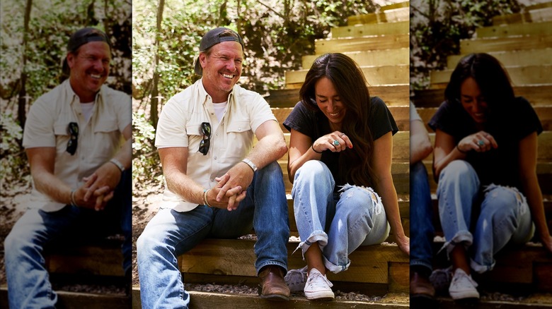 Chip Gaines portant une chemise blanche et un jean avec une casquette à l'envers et Joanna Gaines portant un jean et un t-shirt noir riant ensemble assis dans les escaliers.