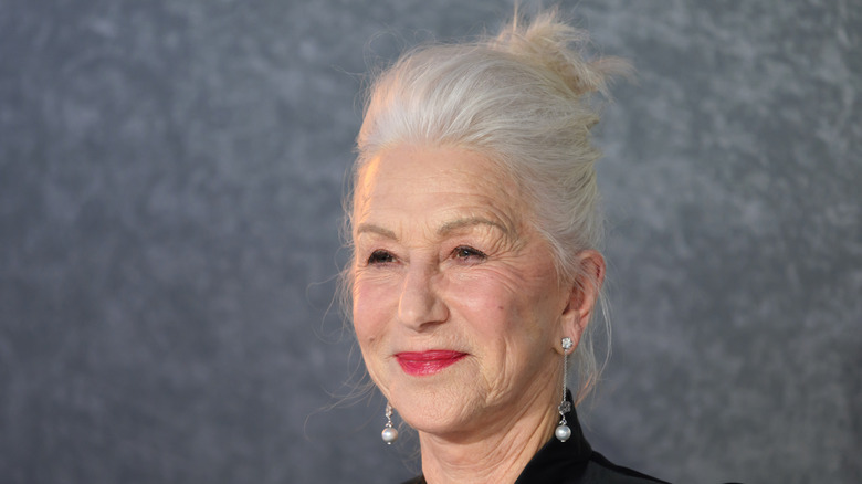 Helen Mirren posant sur un fond gris, portant des boucles d'oreilles pendantes, les cheveux relevés.