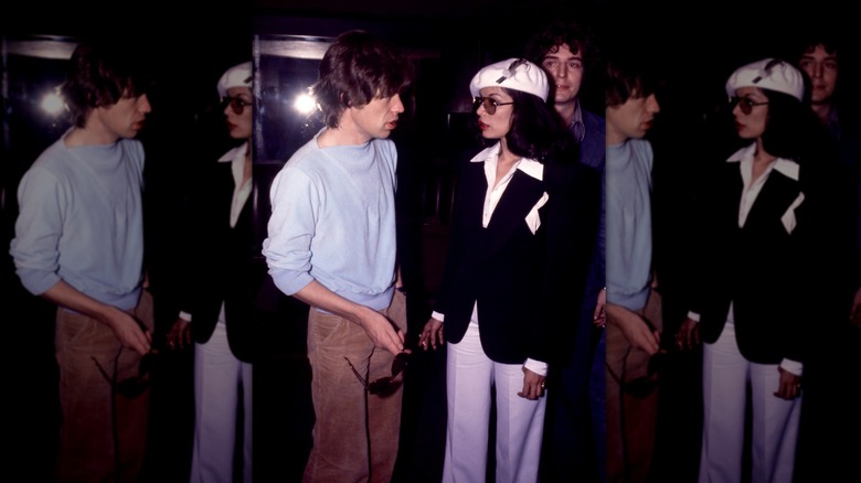 Mick Jagger dans un sweat-shirt bleu et un pantalon en velours côtelé photographié à côté de sa femme Bianca Jagger portant un blazer noir et une casquette blanche.