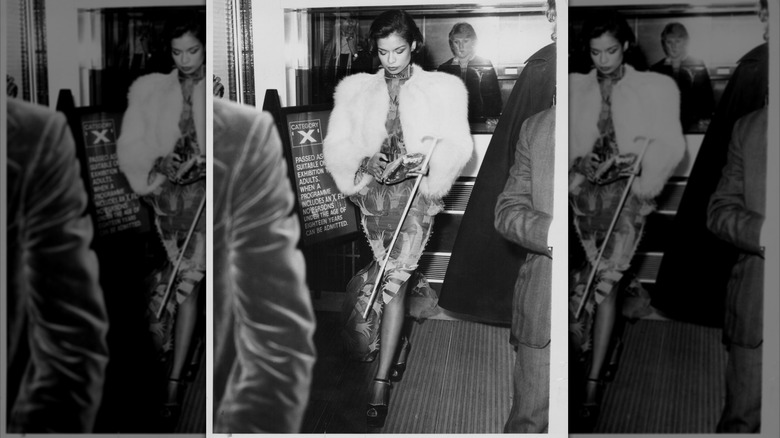 Bianca Jagger regarde vers le bas, vêtue d'un manteau de fourrure blanc et tenant une canne.