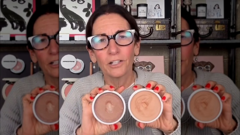 Bobbi Brown porte des lunettes tenant l'un des produits de sa marque, Miracle Balm.