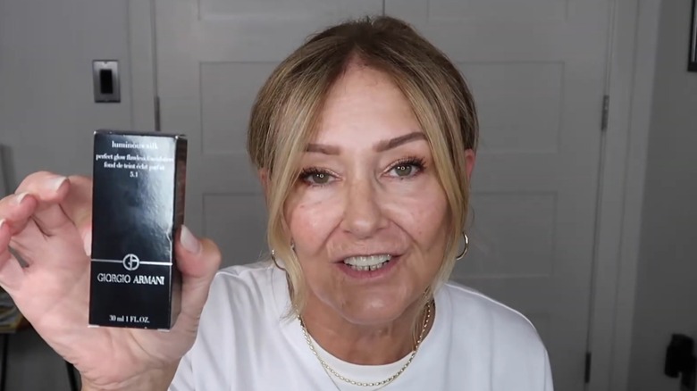 Femme portant un T-short blanc tenant un récipient de Giorgio Armani Luminous Silk Foundation.