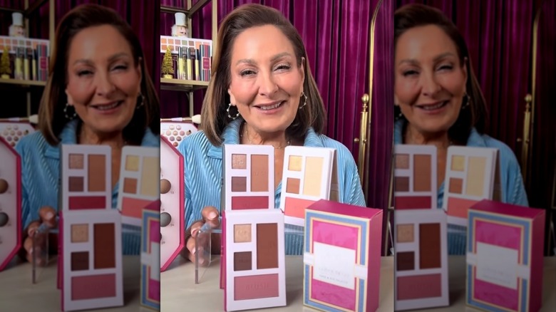 Laura Geller posant avec des palettes de maquillage devant elle.