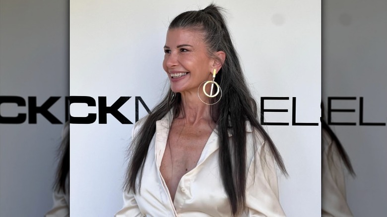 Une femme souriante lors d'un événement avec ses cheveux mi-hauts, portant un chemisier soyeux et des boucles d'oreilles tendance.