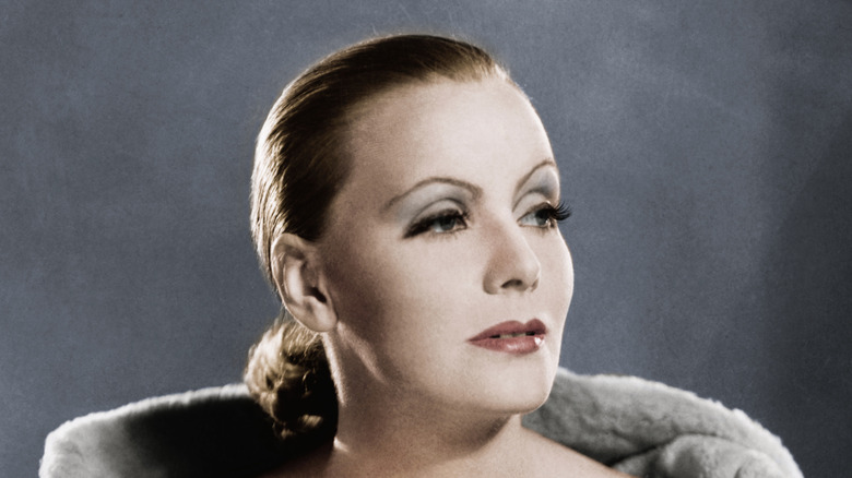 Greta Garbo photographiée portant un chignon bas posant sur un fond gris.
