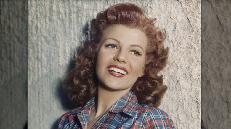 Rita Hayworth souriante dans une chemise à carreaux aux cheveux roux bouclés.