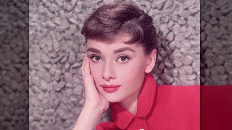 Audrey Hepburn posant avec la tête dans la main et portant un haut rouge