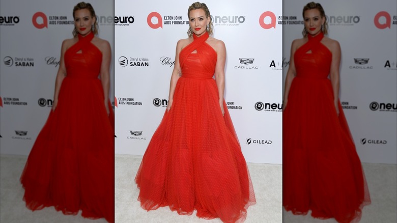 Hilary Duff, les cheveux lissés en arrière, posant lors d'un événement, vêtue d'une robe rouge vif avec une jupe ample.