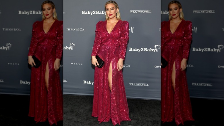 Hilary Duff lors d'un événement sur le tapis rouge posant dans une robe rouge scintillante avec un décolleté en V profond et une jupe fendue.