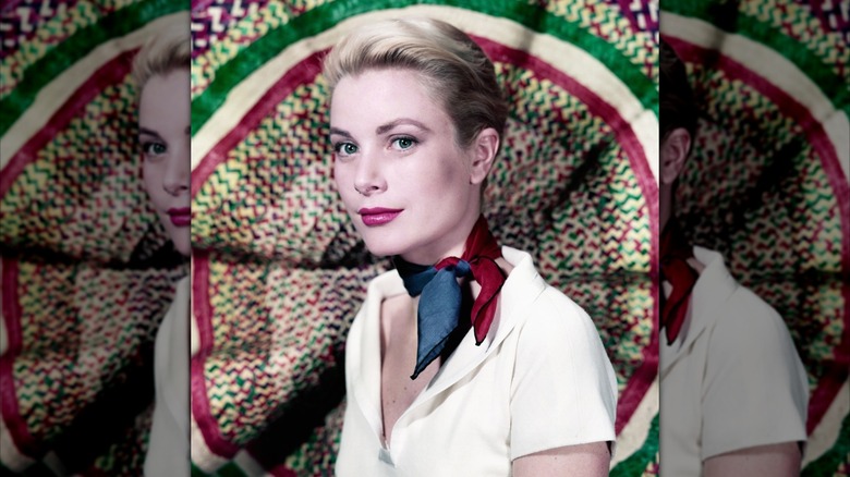 Grace Kelly les cheveux relevés, vêtue d'une chemise blanche et d'un foulard bleu et rouge devant un fond coloré.