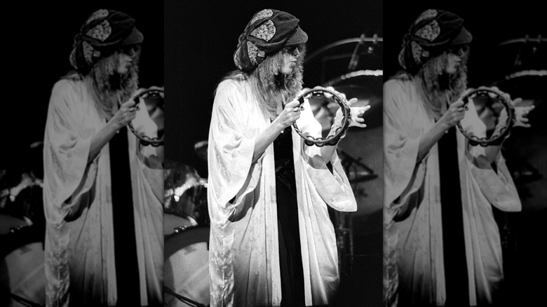 Photo en noir et blanc de Stevie Nicks portant un chapeau souple et une robe blanche jouant du tambourin avec Fleetwood Mac en 1977.