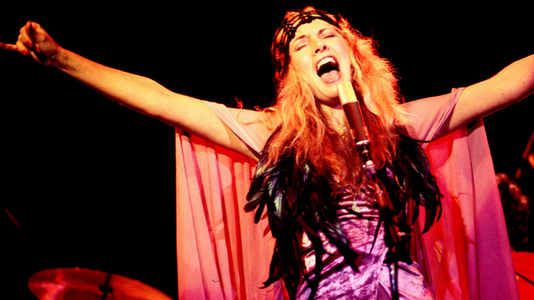 Stevie Nicks, les bras tendus, chantant vêtue d'une cape fluide et d'une tenue à plumes, jouant avec Fleetwood Mac en 1978.