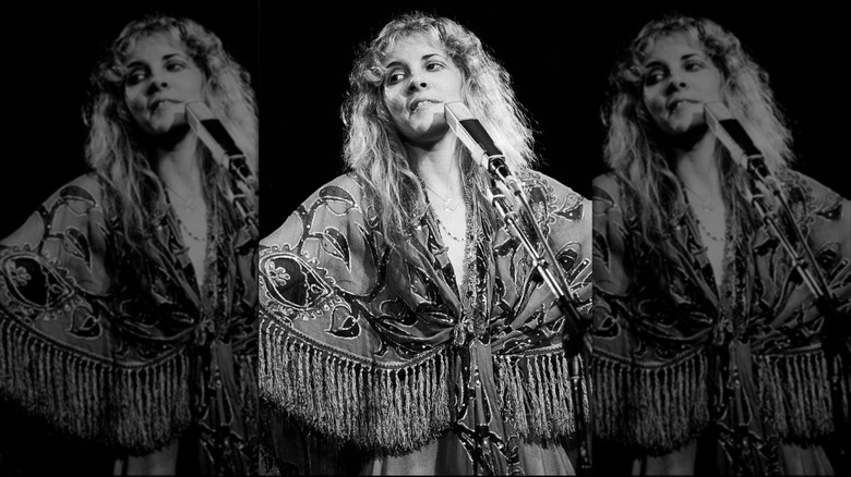 Photo en noir et blanc de Stevie Nicks devant un micro portant un haut à franges motif cachemire en train de jouer avec Fleetwood Mac en 1978.