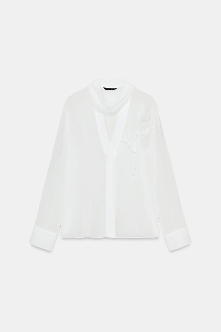 Blouse blanche semi-transparente avec broderie de fleurs.
