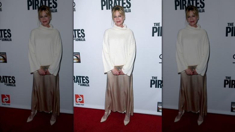 Melanie Griffith sourit en portant un col roulé blanc et une jupe en satin beige