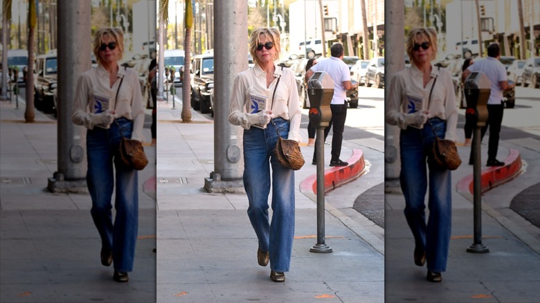 Melanie Griffith tient un livre et porte un jean large et un chemisier blanc.