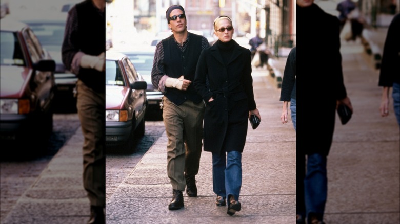 Carolyn Bessette-Kennedy en jean bootcut, trench-coat noir et bottes à talons marchant aux côtés de JFK Jr.