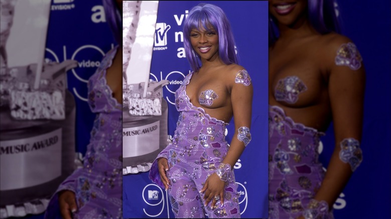 Lil Kim aux MTV VMA 1999 avec une combinaison lavande ornée et un sein dépassant recouvert d'un cache-téte violet.
