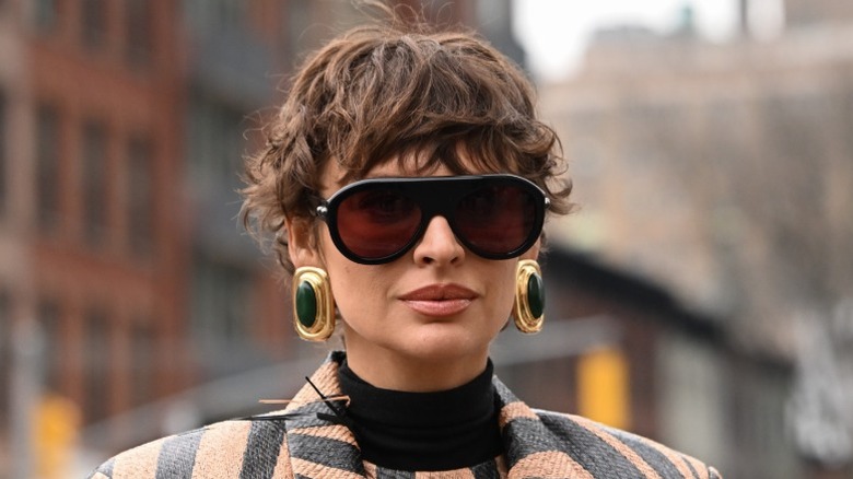 Une femme portant des lunettes de soleil, de grandes boucles d'oreilles et ses cheveux coupés en forme de lutin ondulé
