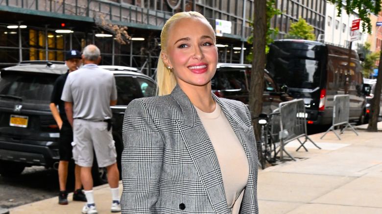 Hayden Panettiere marchant dehors, coiffée en queue de cheval et portant un blazer à carreaux noir et blanc.