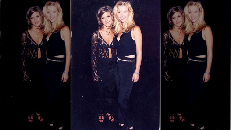 Lisa Kudrow en pantalon noir et mini-gilet noir posant à côté de Jennifer Aniston.