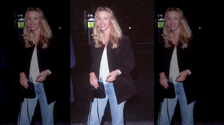 Lisa Kudrow porte un jean, une chemise blanche et une veste noire, avec de longs cheveux ondulés.