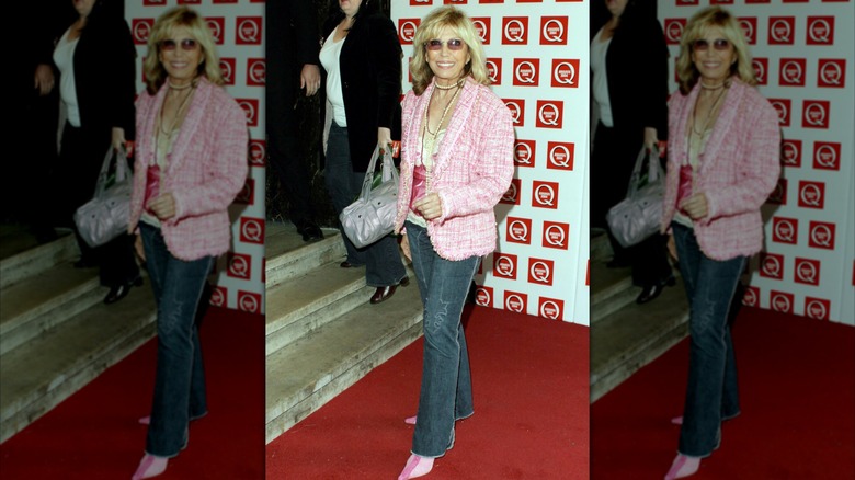 Nancy Sinatra posant sur un tapis rouge portant un jean foncé avec un blazer rose et des chaussures roses.