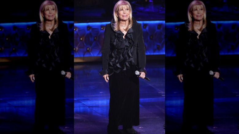 Nancy Sinatra tenant un micro sur scène, vêtue d'un haut noir à volants et d'une jupe noire.