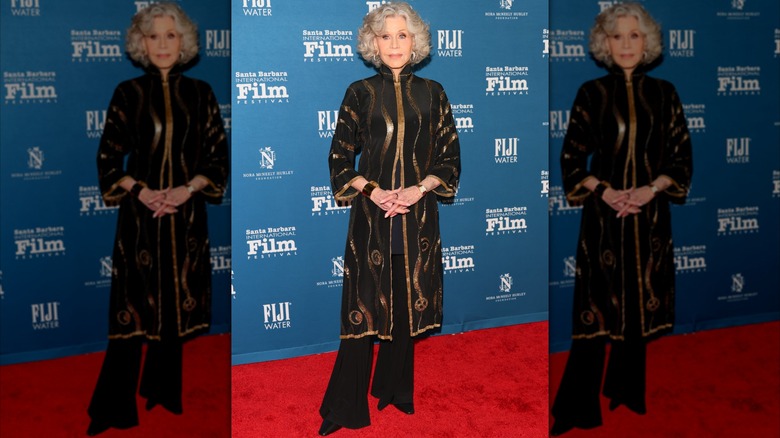 Jane Fonda posant lors d'un événement sur le tapis rouge, portant un pantalon noir fluide et une tunique noir et or.