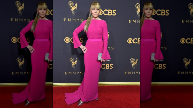 Jane Fonda posant sur le tapis rouge vêtue d'une robe rose vif avec ses cheveux en queue de cheval basse avec une frange émoussée.