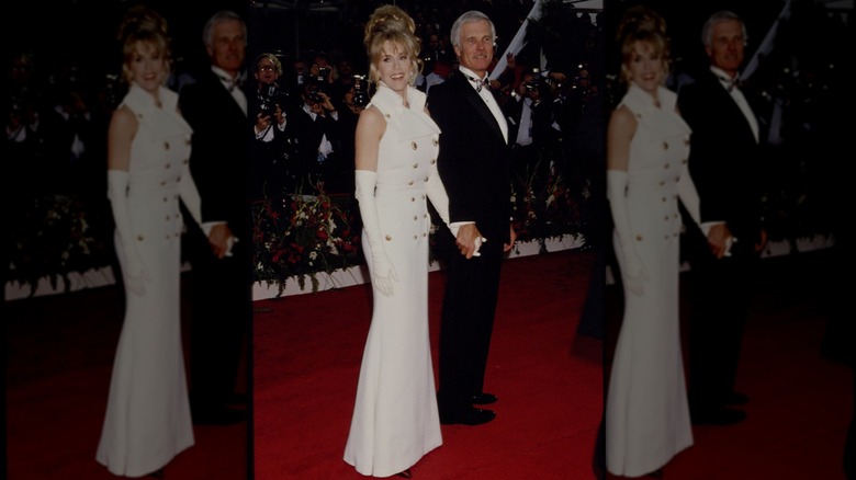 Jane Fonda posant sur le tapis rouge des Oscars, vêtue d'une robe blanche avec des boutons dorés et de longs gants blancs.