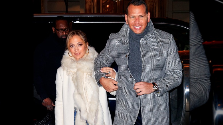 Jennifer Lopez dans un manteau de fourrure blanc tenant Alex Rodriguez vêtu d'un caban gris.