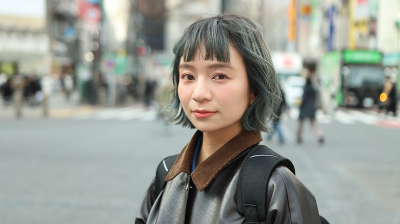 Femme marchant dans une ville portant une veste en cuir noire et un bob gris vécu.