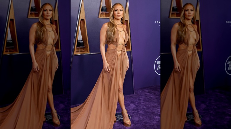 Jennifer Lopez sur le tapis rouge vêtue d'une longue robe beige avec des découpes et des détails métallisés.