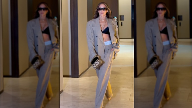 Jennifer Lopez marchant et portant un ensemble pantalon et veste beige avec un haut soutien-gorge noir, une pochette à imprimé léopard et des lunettes de soleil.