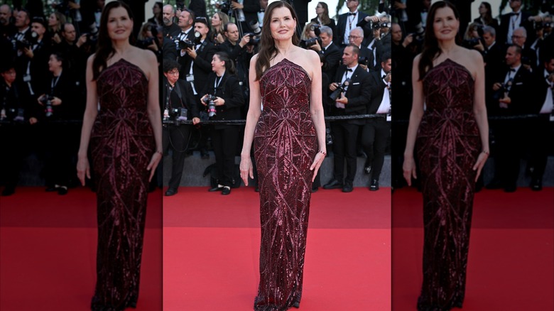 Geena Davis posant sur le tapis rouge vêtue d'une robe bustier rouge vin avec des motifs de paillettes complexes.