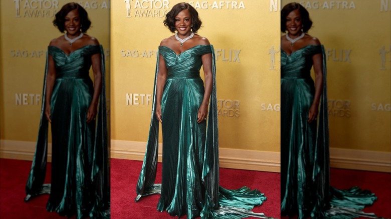 Viola Davis posant sur le tapis rouge dans une robe vert émeraude brillante à épaules dénudées avec des détails plissés et une traîne.