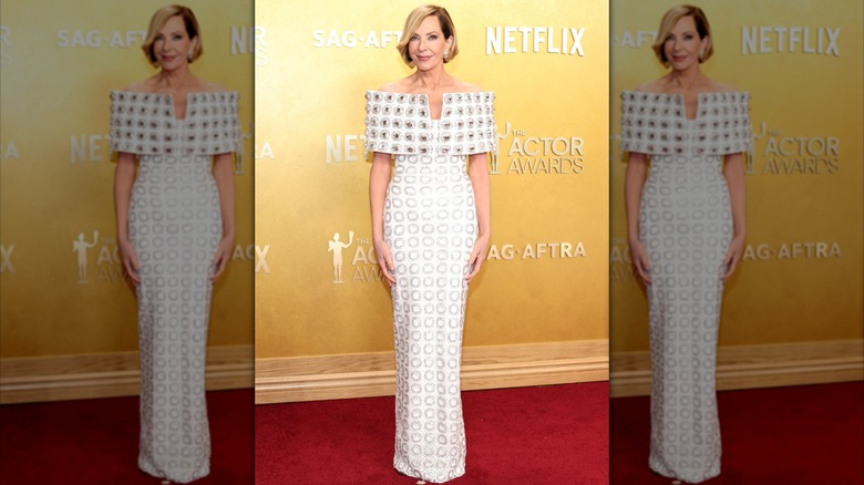 Allison Janney posant sur le tapis rouge dans une robe blanche à imprimé géométrique et épaules dénudées.