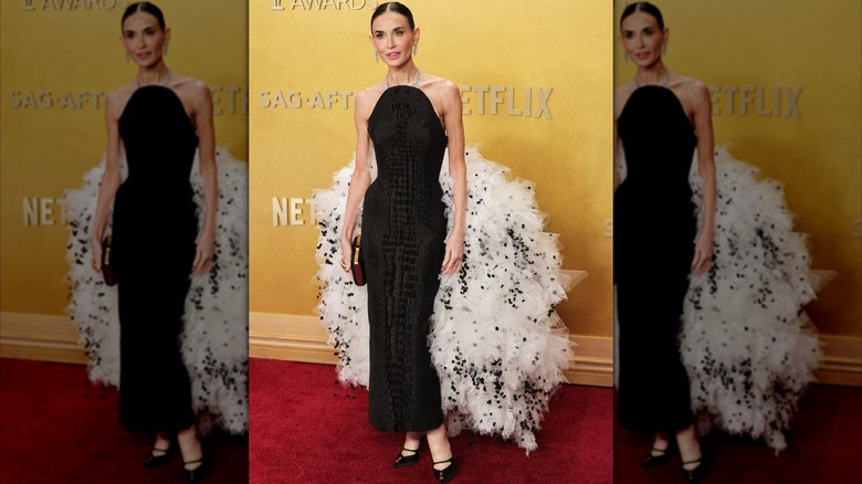 Demi Moore posant sur le tapis rouge dans une robe dos nu noire avec une traîne moelleuse blanche et noire.