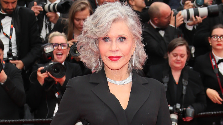 Jane Fonda posant lors d'un événement sur le tapis rouge portant du rouge à lèvres, une veste noire et un collier de diamants.