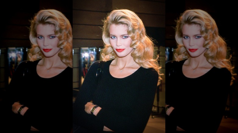 Claudia Schiffer posant dans un haut noir à encolure dégagée avec du rouge à lèvres, les bras croisés et les cheveux blonds bouclés usés.