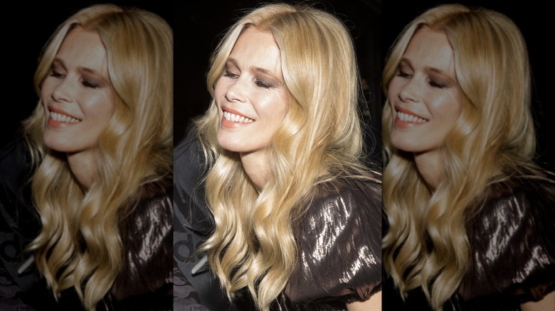 Claudia Schiffer souriante, les yeux fermés dans un haut métallique brillant et ses cheveux bouclés lâchés.