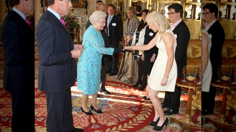 Ellie Goulding, vêtue d'une robe blanche avec des chaussures noires, fait la révérence et serre la main de la reine Elizabeth, vêtue d'une robe bleue.